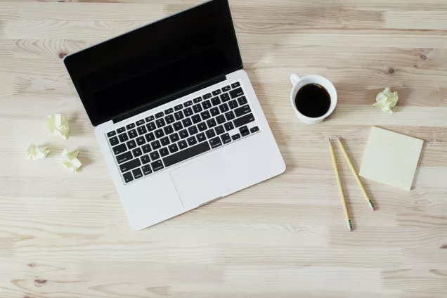 A laptop, a cup of coffee, some pencils and post-it's seen from above. Photo.